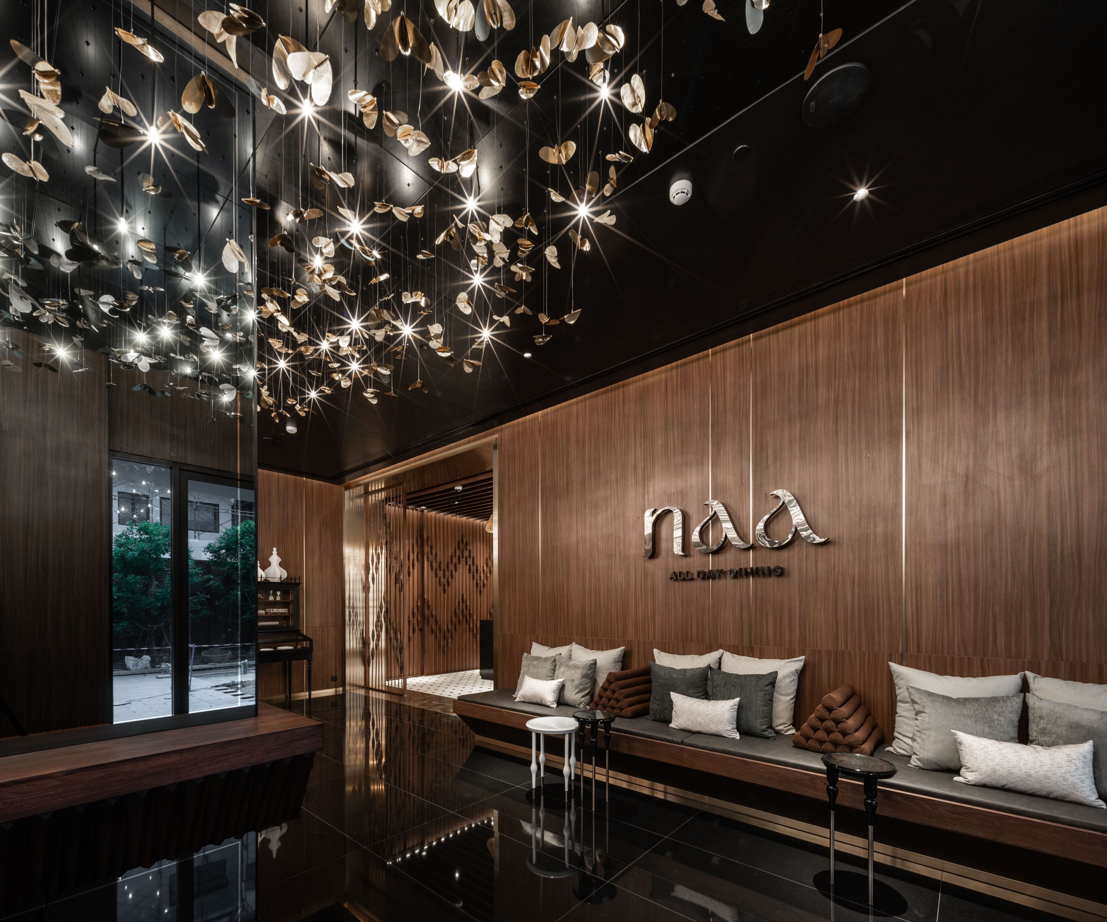 A modern interior with a wooden wall, a seating area with cushions, and a ceiling with hanging light fixtures.