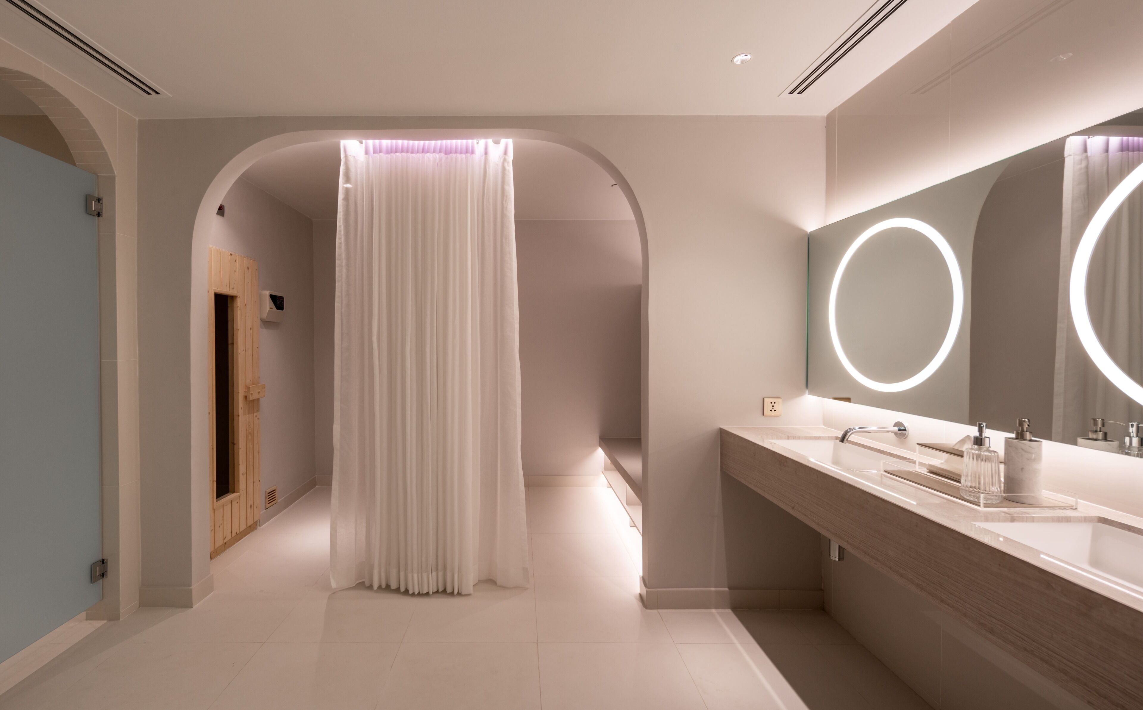 Un baño moderno con tocador, un espejo grande con luces circulares y una zona de ducha con cortina.