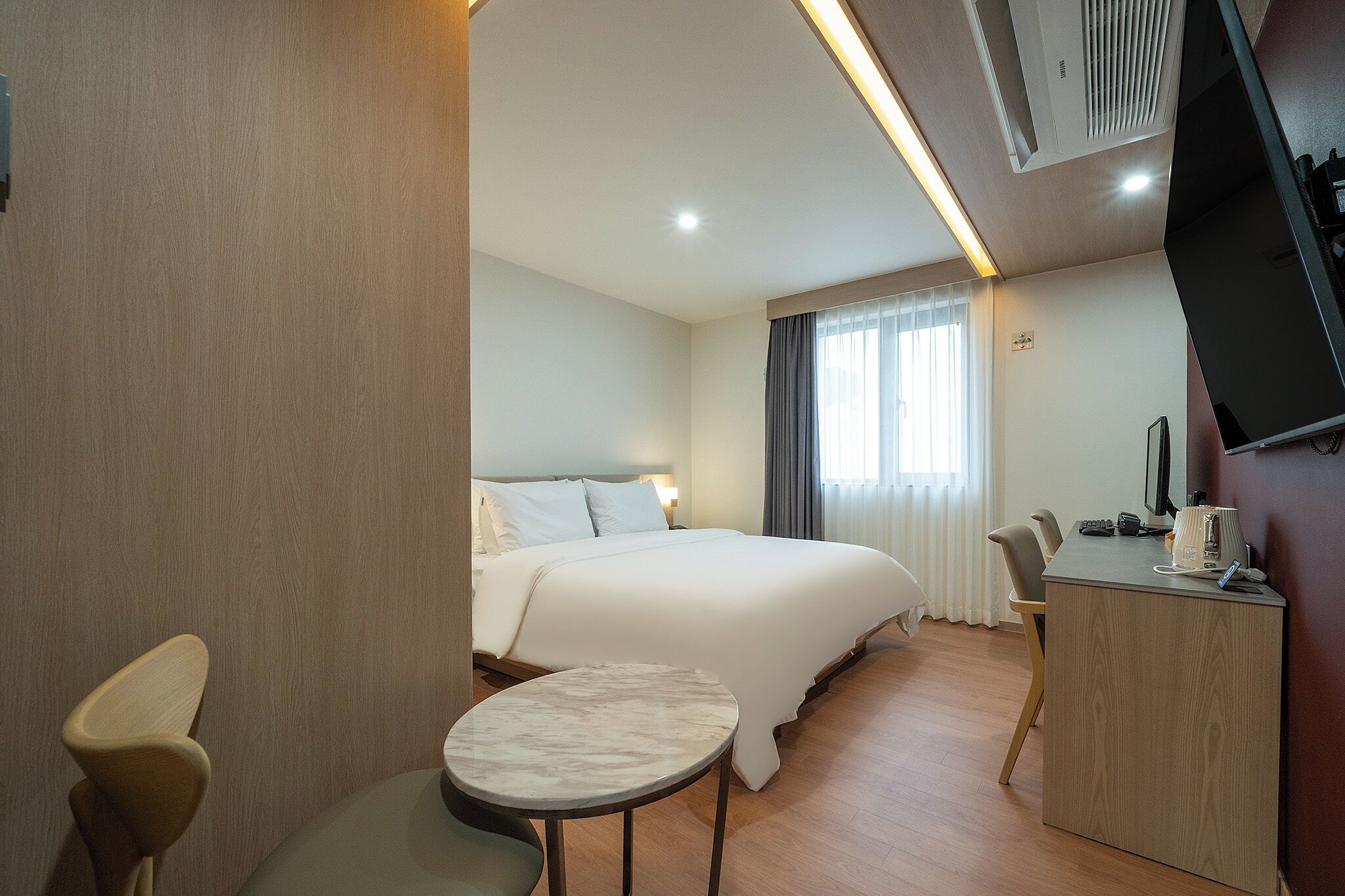 A hotel room with a bed, a desk, a chair, a small table, and a TV.