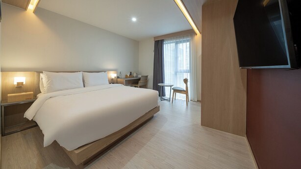 Una habitación de hotel moderna con una cama grande, mesitas de noche con lámparas, un escritorio, una silla y un televisor.