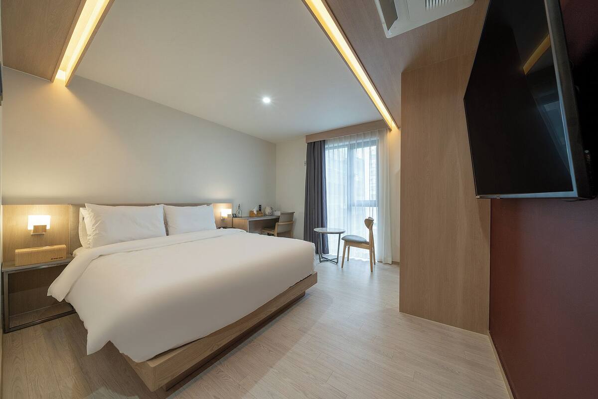 Een moderne hotelkamer met een groot bed, nachtkastjes met lampen, een bureau, een stoel en een televisie.