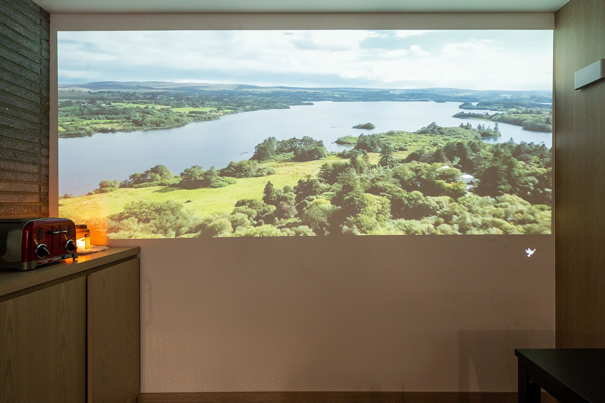 A projection of a scenic landscape with a lake, surrounded by greenery and hills.