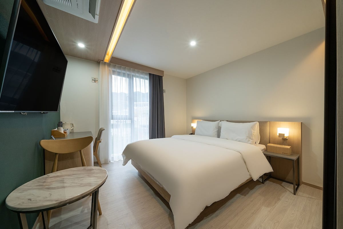 Een hotelkamer met een bed, nachtkastje, stoel en een klein tafeltje.