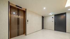 Un ascensor con pantalla digital, una puerta con placa de número y una pared lisa con interruptor de luz.