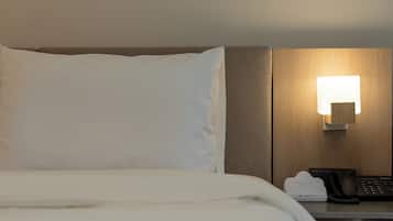 A hotel room with a bed, a bedside table with a lamp, a telephone, and a hotel-branded device.