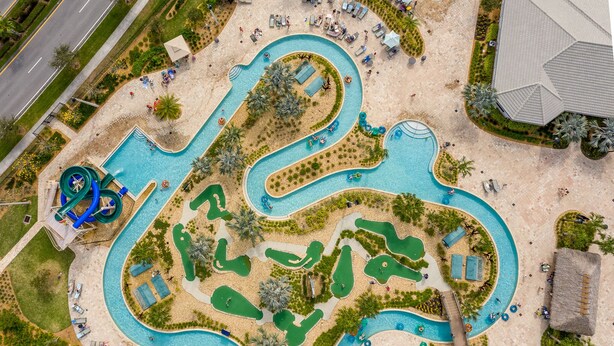Eine Luftaufnahme eines Resorts mit einem gewundenen Pool, mehreren Liegebereichen und einem großen Gebäude.