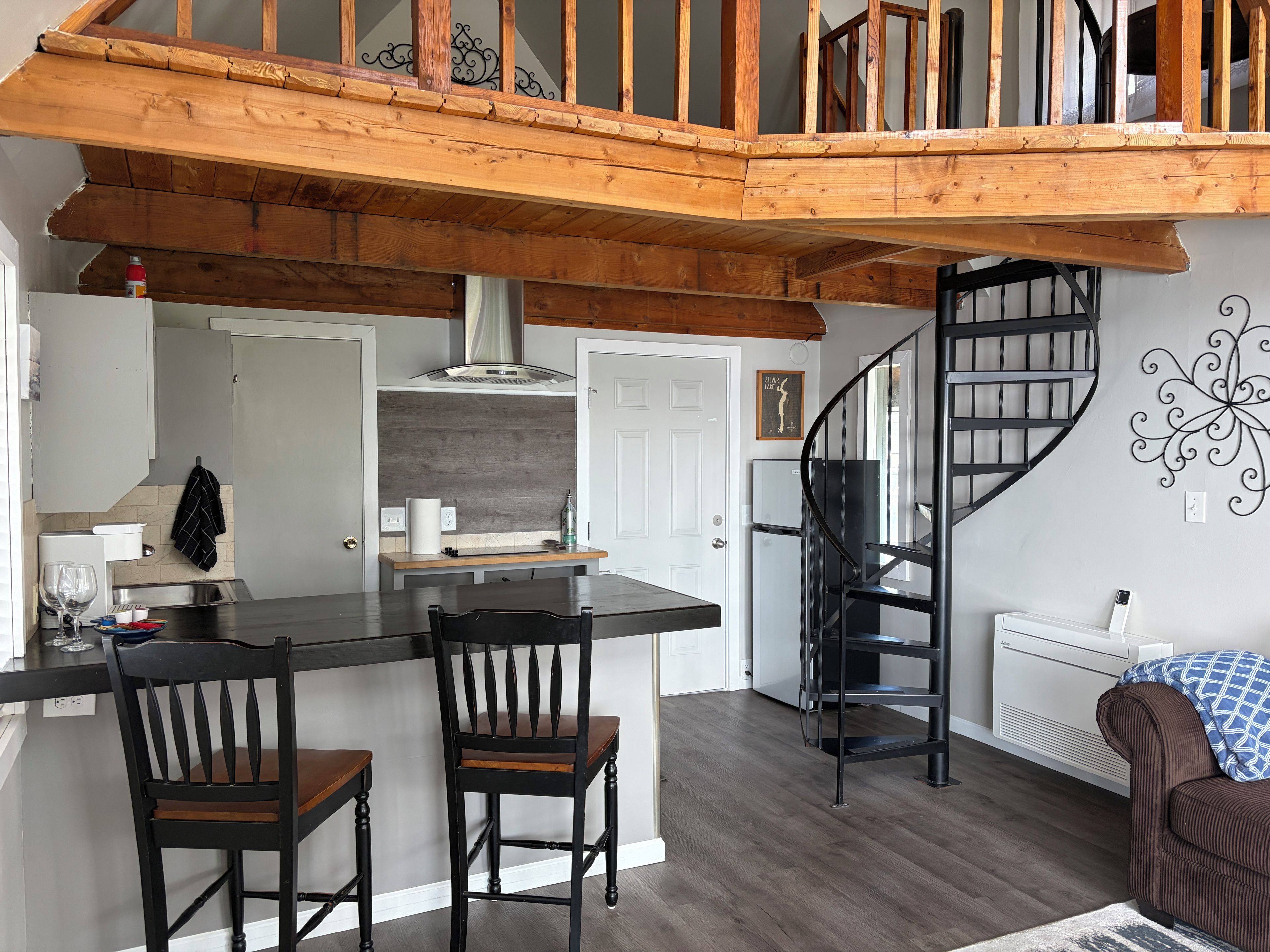 A modern kitchen with a wooden ceiling, a black spiral staircase, and a dining area with two chairs.