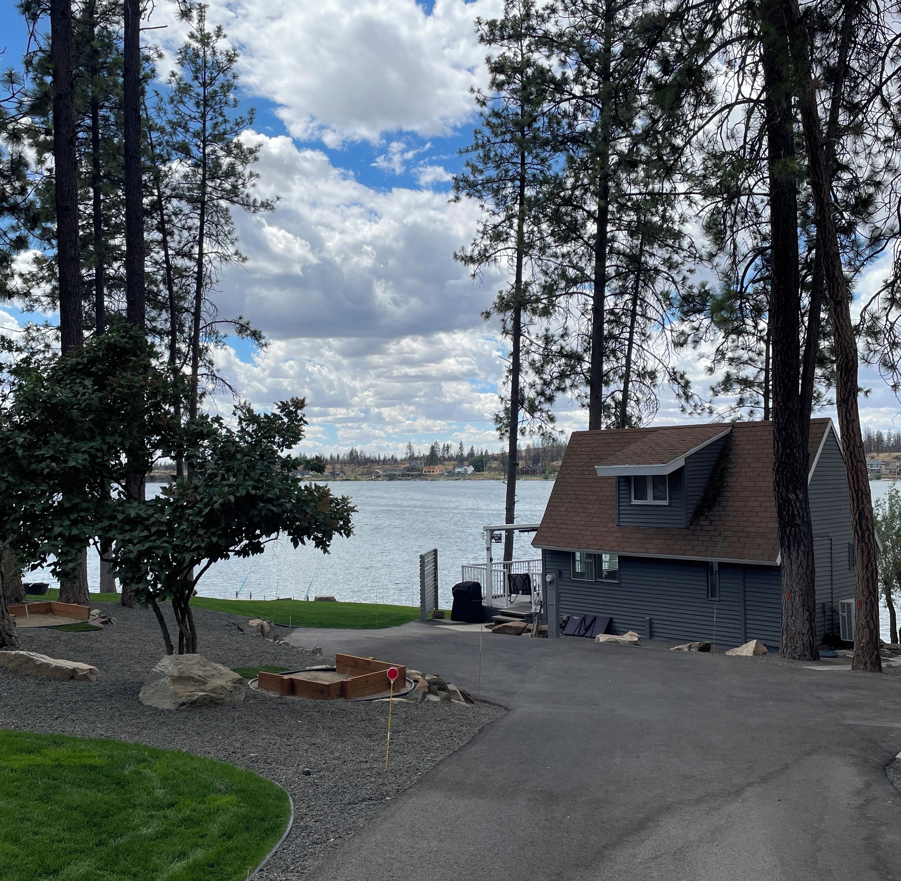 Una cabaña junto al lago con un muelle, rodeada de altos árboles y una vista despejada del lago.