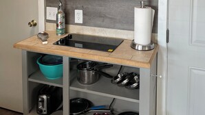 Una cocina compacta con estufa integrada, extractor de acero inoxidable, un lavamanos pequeño y una variedad de utensilios de cocina guardados en estantes.