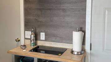 A compact kitchen with a built-in stove, a stainless steel range hood, a small sink, and a variety of cookware stored on shelves.