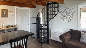 Una cocina con techo de madera, una escalera espiral negra, un refrigerador, una mesa de comedor con sillas y un adorno en la pared.