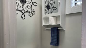A bathroom with a toilet, a shelf with cleaning products, and a decorative metal wall piece.