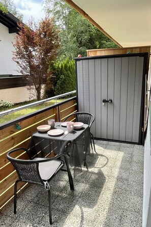 A balcony with a table and chairs, a door, and a view of trees and a building. - Am Birkenhain by Interhome (Seefeld in Tirol)