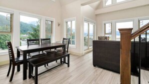 A spacious room with a large dining table, multiple chairs, a dark sofa, and a staircase. - Harrison Hot Springs (Harrison Hot Springs)