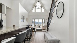 A modern kitchen with a bar area, a dining space, and a staircase leading to a loft bedroom. - Harrison Hot Springs (Harrison Hot Springs)