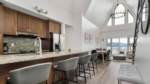 A modern kitchen with a large island, bar stools, and a dining area with a view. - Harrison Hot Springs (Harrison Hot Springs)