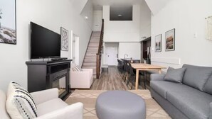 A modern living room with a fireplace, a flat-screen TV, and a staircase leading to an upper level. - Harrison Hot Springs (Harrison Hot Springs)