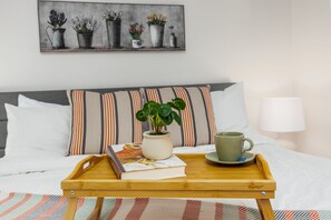 A neatly made bed with a striped pillow, a bedside table with a tray holding a book, a mug, and a potted plant. - W House in BLS, Game Room, Fire Pit, Hot Tub, Central AC&Heat, Pet friendly! (Arnold)