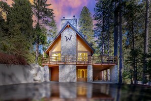 A modern log cabin with a stone facade, wooden balcony, and a stone entrance. - W House in BLS, Game Room, Fire Pit, Hot Tub, Central AC&Heat, Pet friendly! (Arnold)