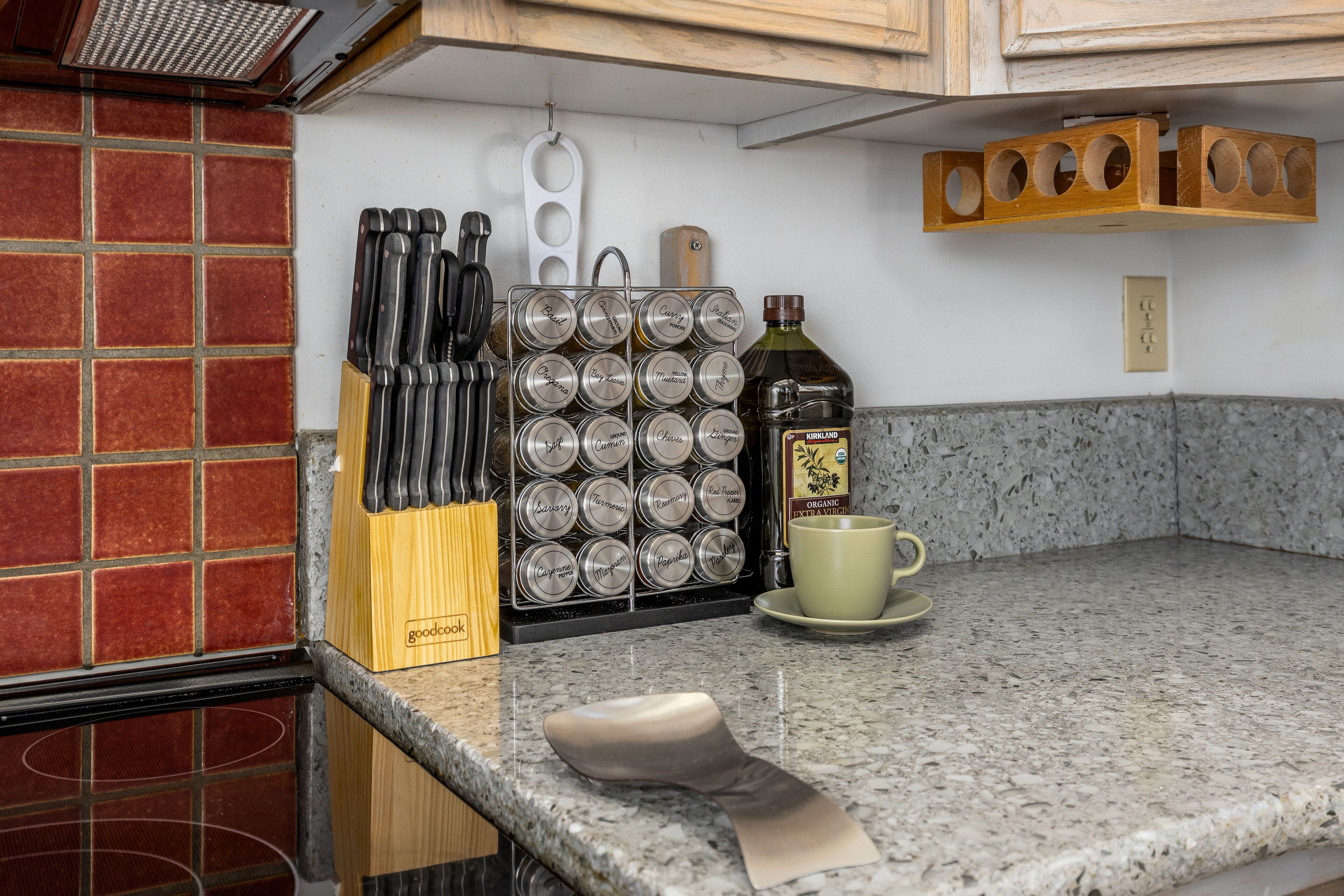 A kitchen counter with a knife block, spice jars, a bottle of olive oil, and a coffee cup.