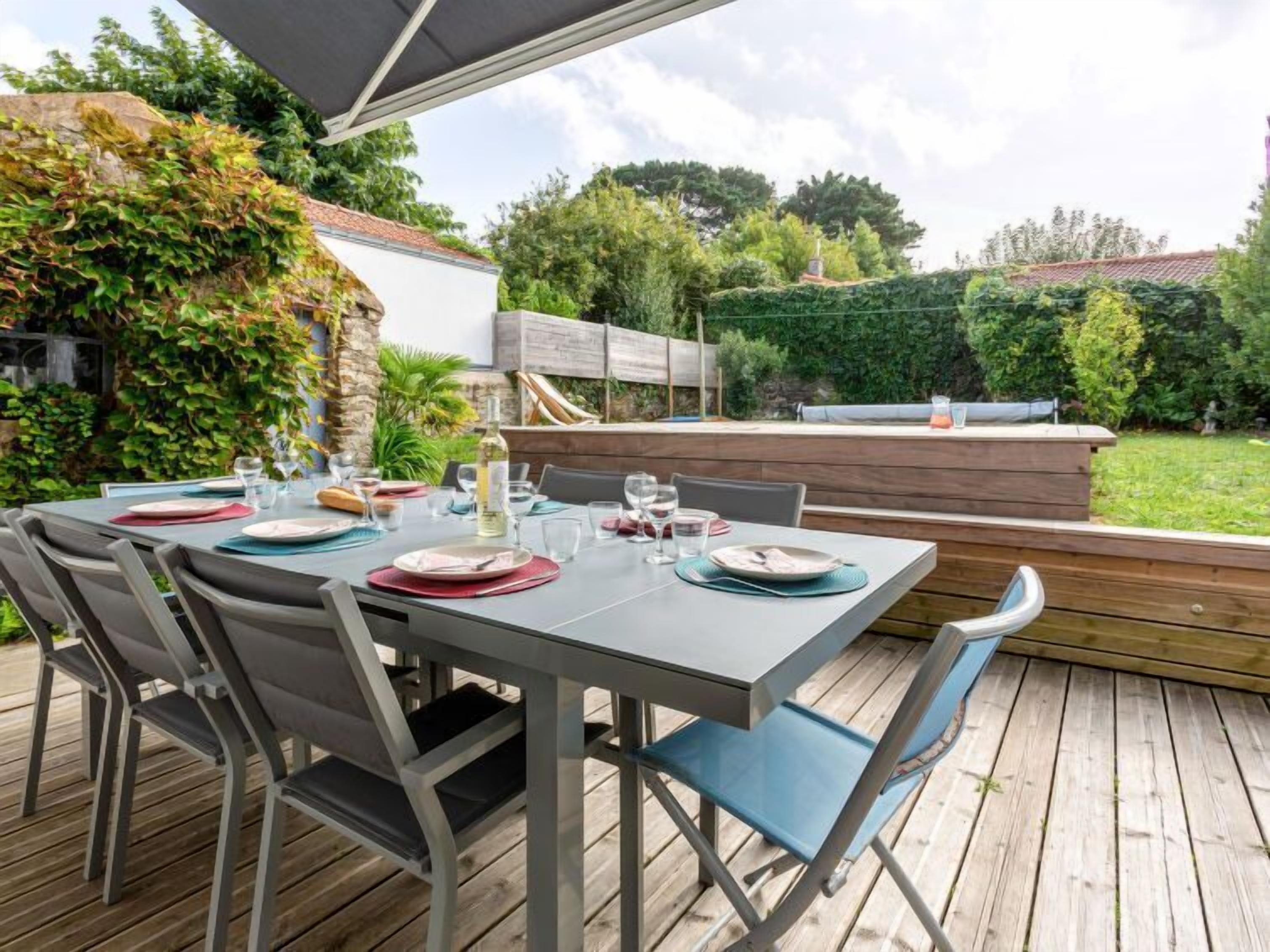 An outdoor dining area with a table set for six, surrounded by chairs, and a wooden deck.