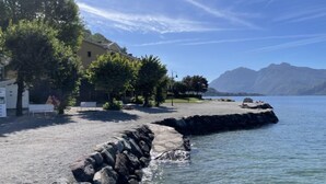 A coastal area with a rocky shoreline, a bench, and a building with a sloped roof. - Punta Grumo 2 by Interhome (Lierna)