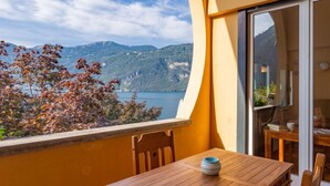 A balcony with a wooden table and chairs, overlooking a lake and mountains. - Punta Grumo 2 by Interhome (Lierna)
