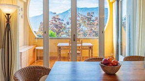 A dining area with a table, chairs, and a bowl of fruit. There is a view of mountains through a glass door. - Punta Grumo 2 by Interhome (Lierna)