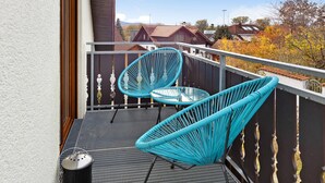 Un balcon avec deux chaises bleues, une petite table et un gril en métal.