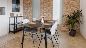 Un coin repas comprenant une table, des chaises, un vase avec des fleurs, une plante en pot et un mur en briques.