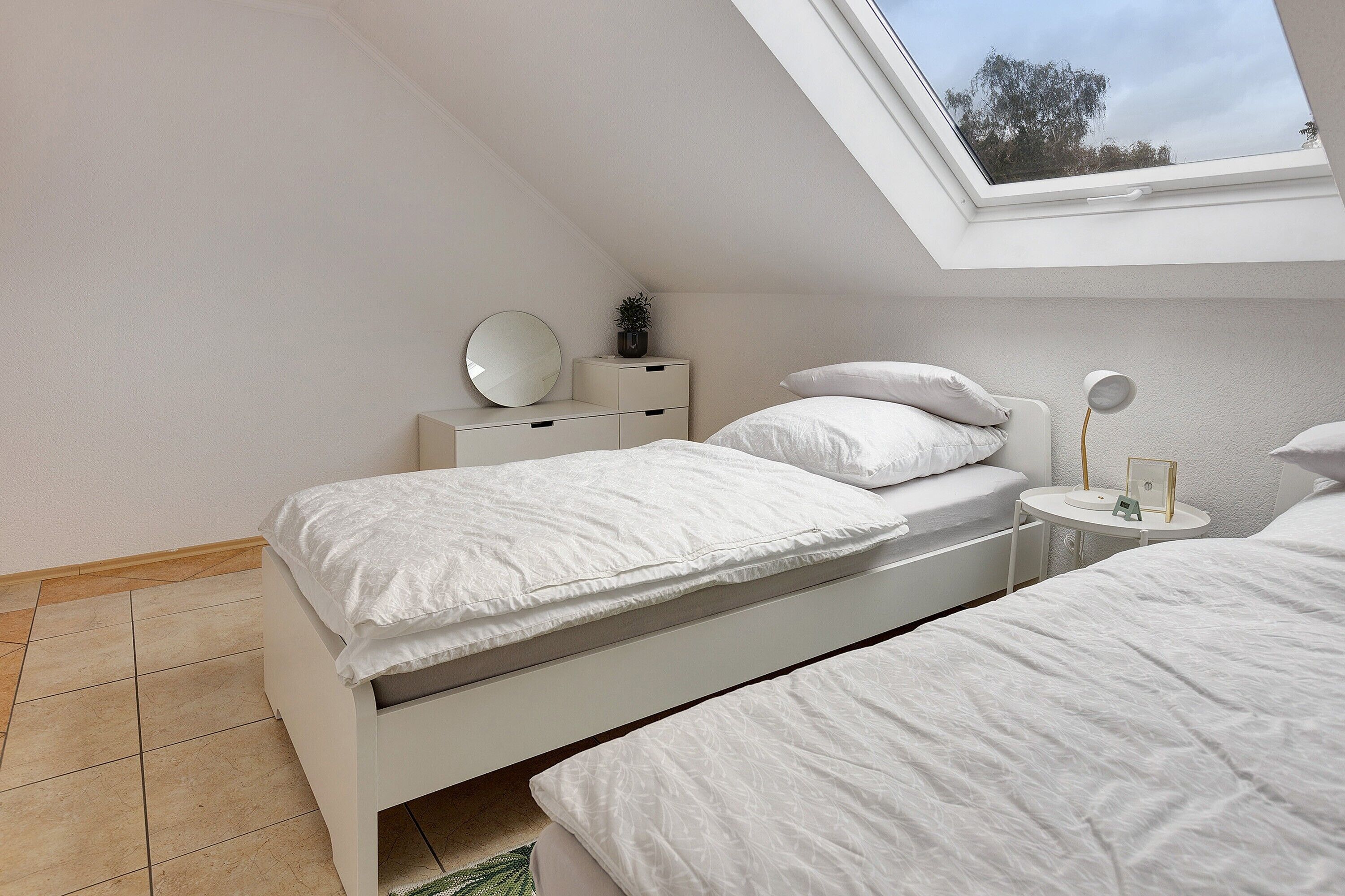 Een slaapkamer met twee bedden, een dakraam, een nachtkastje met een lamp en een kleine plant.
