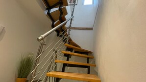 Portaat, joissa on puiset askelmat ja metallikaiteet, pieni ikkuna yläosassa ja ruukkuistutettu kasvi vasemmalla puolella.