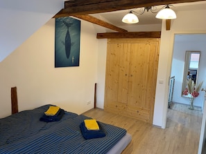 A bedroom with a bed, a wooden wardrobe, a painting of a whale, and a mirror reflecting a room with flowers. - Apartment "Happynest" with Balcony & Wi-Fi (Jena)