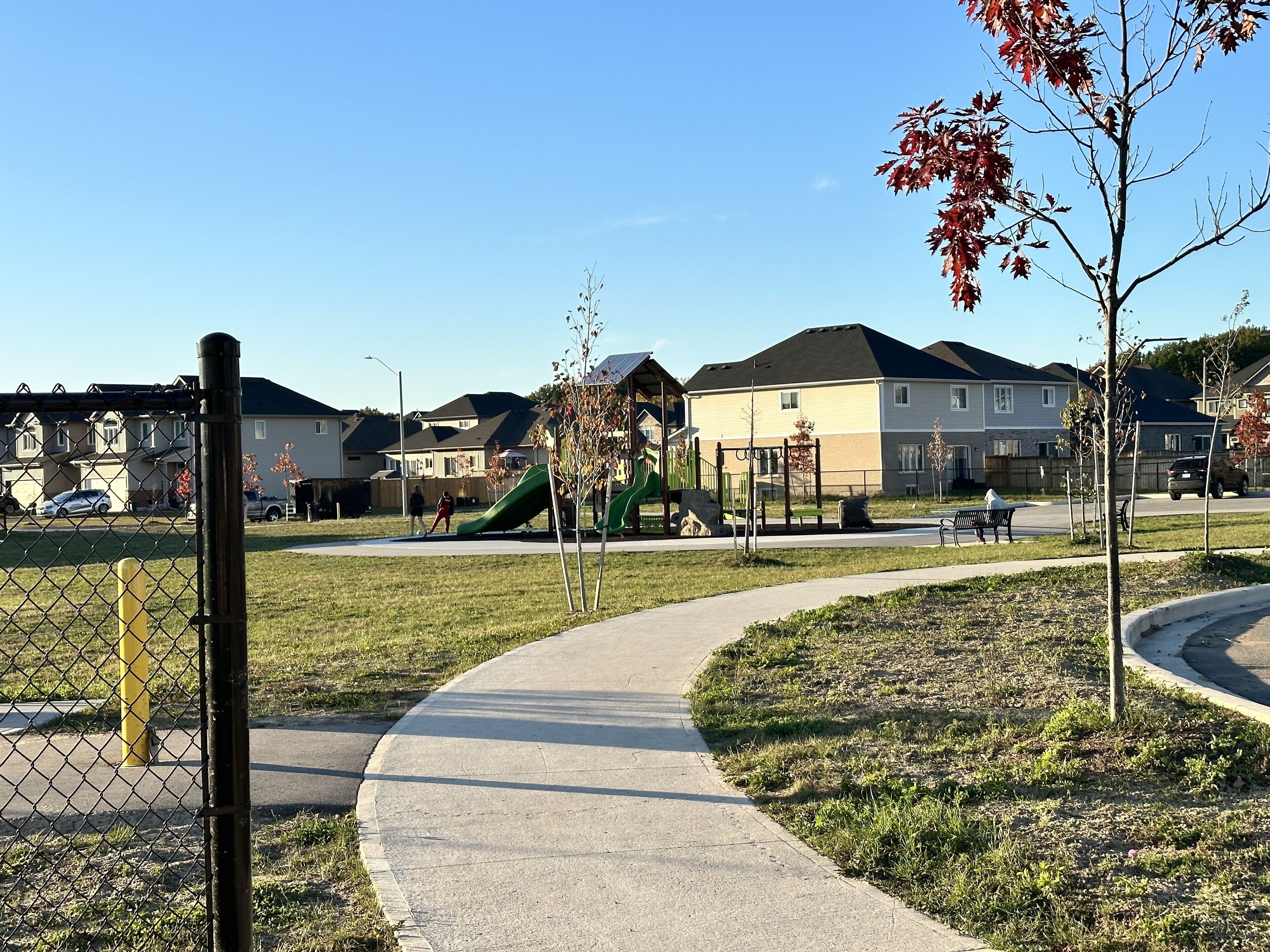 A residential area with a playground, a curved pathway, and houses in the background.