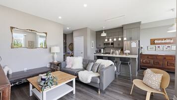 A modern living room with a sofa, coffee table, and a dining area with a kitchen in the background.