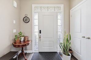 A hallway with a white door, a clock, a small table with plants, and a potted plant beside the door.
