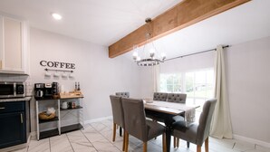 Une cuisine moderne dotée d’un coin café, d’un espace repas avec une table et des chaises, et d’une grande fenêtre agrémentée de rideaux.