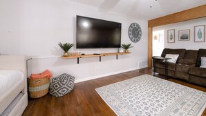 Un salon moderne avec un téléviseur à écran plat fixé au mur, un ventilateur de plafond, une étagère en bois ornée d’objets décoratifs, un tapis à motifs et un canapé en cuir marron.