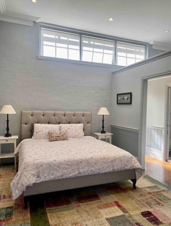 A bedroom with a large bed, two bedside tables with lamps, a patterned bedspread, and a view of the outside through a window. - Mrs McCall’s General Store (BLACKHEATH)