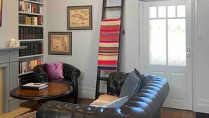 Una sala de estar con un sofá de cuero, una mesa de centro, una estantería, una escalera y una puerta con ventanal.