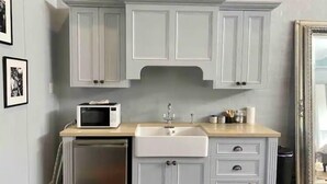 Una cocina con armarios blancos, un microondas, un fregadero y un refrigerador pequeño.