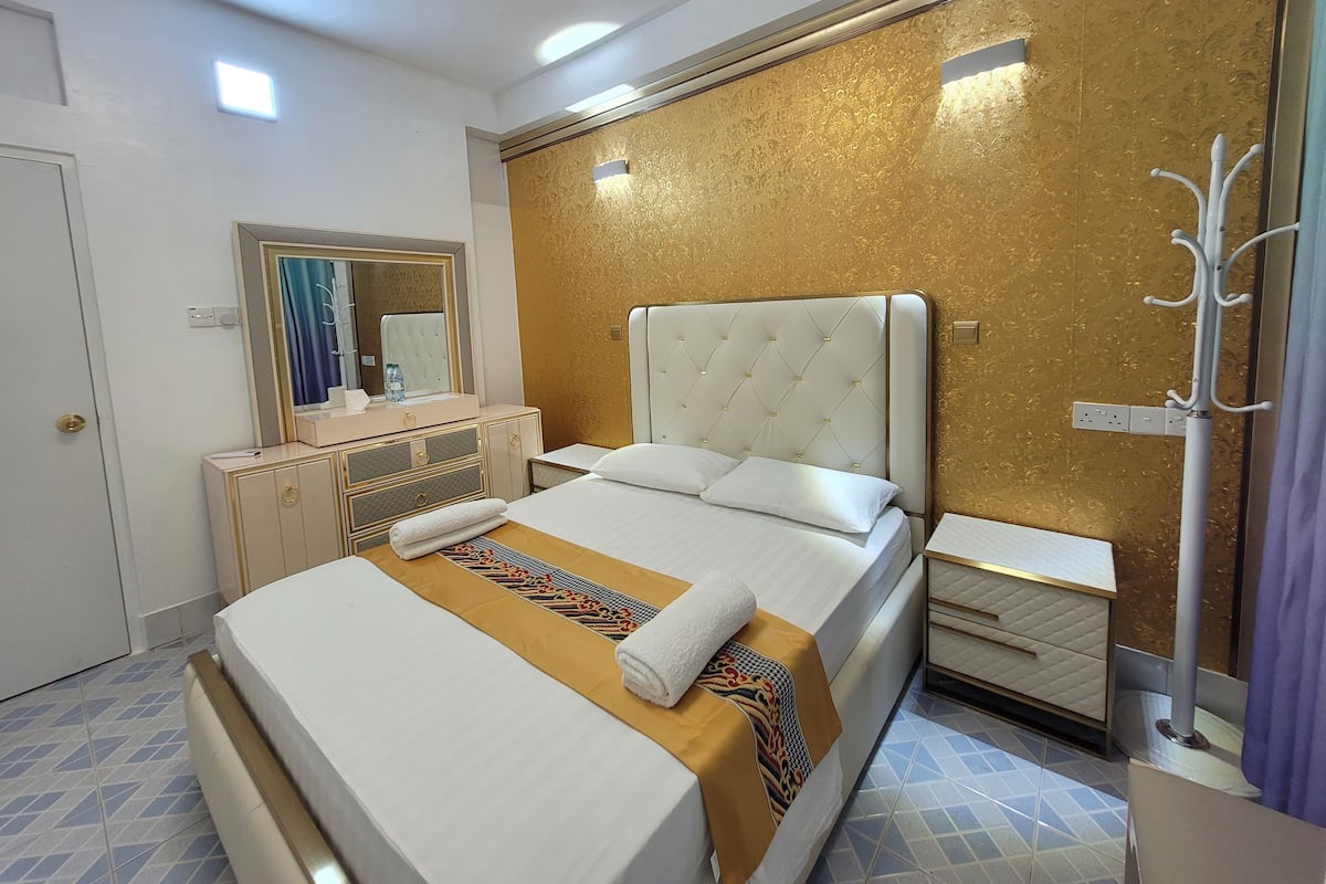 Habitación de hotel con una cama grande, una tocador con espejo y una pared con diseño dorado.