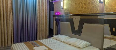 A hotel room with a large bed, a bedside table, an air conditioning unit, and a mirror.