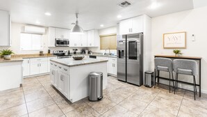 A modern kitchen with white cabinets, stainless steel appliances, a central island, and a bar area with two stools. - Keirland Kottage (Scottsdale)