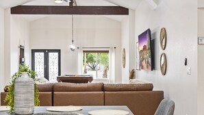 A spacious living area with a brown sectional sofa, a dining table with placemats, a large vase with greenery, and a painting on the wall. - Keirland Kottage (Scottsdale)