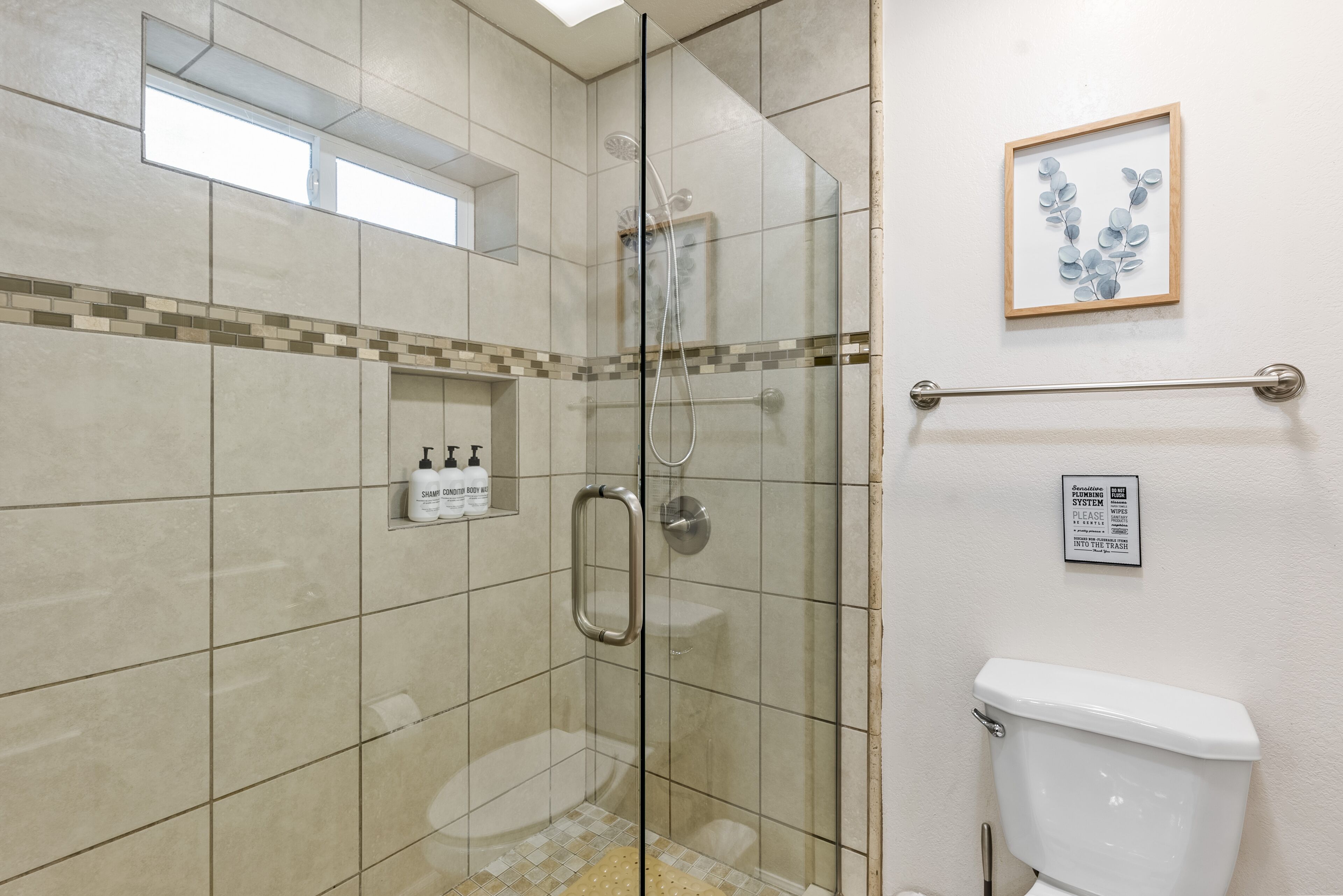 A glass-enclosed shower area with a handrail, a toilet, and a framed artwork on the wall.