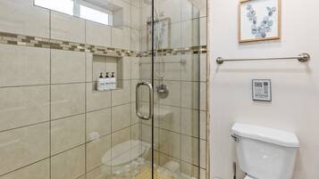 A glass-enclosed shower area with a handrail, a toilet, and a framed artwork on the wall.