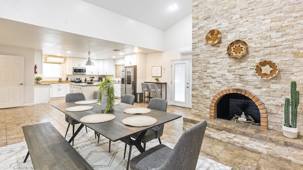 A spacious dining area with a large table and chairs, a kitchen in the background, and a stone fireplace with decorative plates. - Keirland Kottage (Scottsdale)