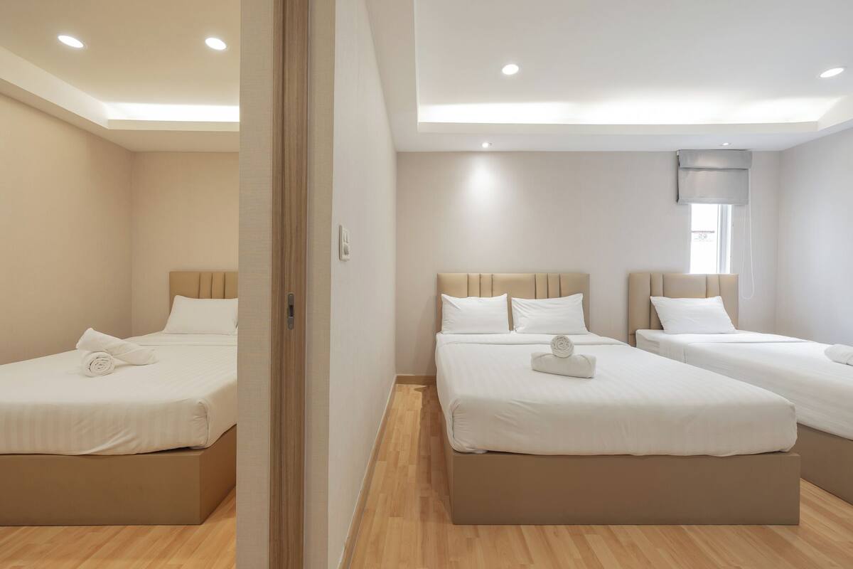 A hotel room with three beds, a large window with a blind, and a ceiling with recessed lighting.