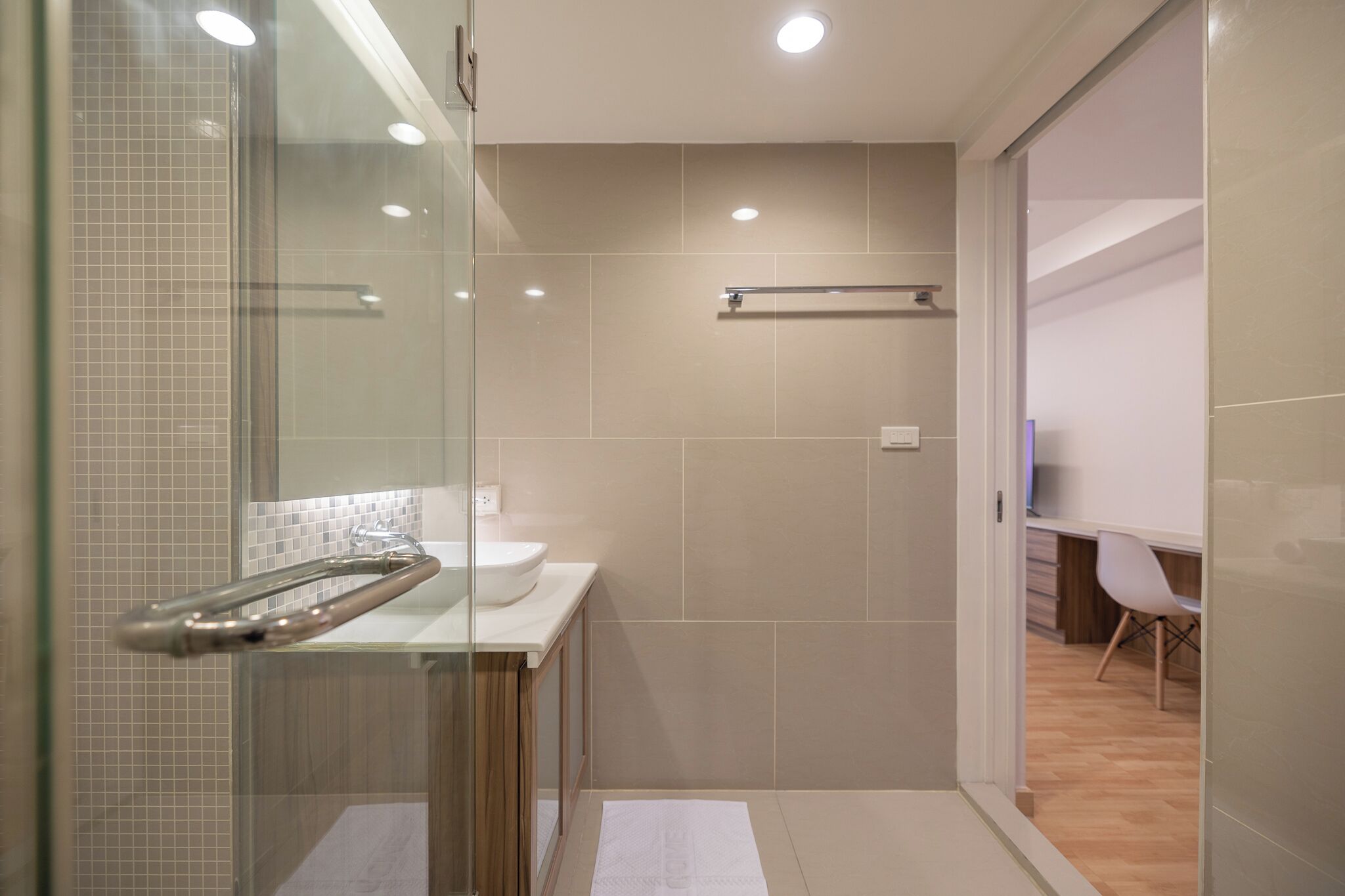 A modern bathroom with a glass shower enclosure, a white sink, and a wooden vanity.